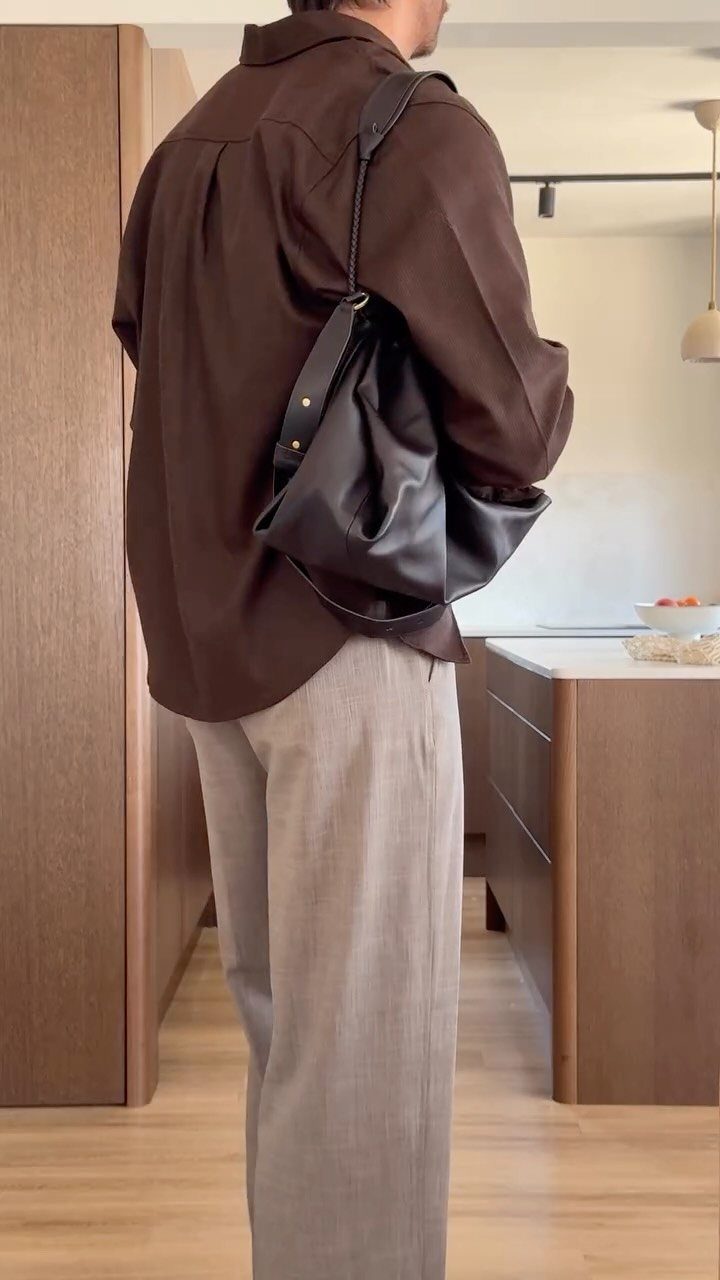 Man wearing a brown collared shirt and grey trousers with a black leather bag.
