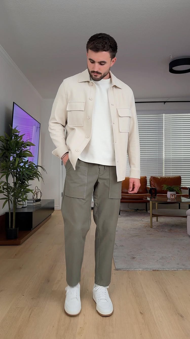 Man wearing a cream overshirt, white t-shirt, olive cargo pants, and white sneakers.