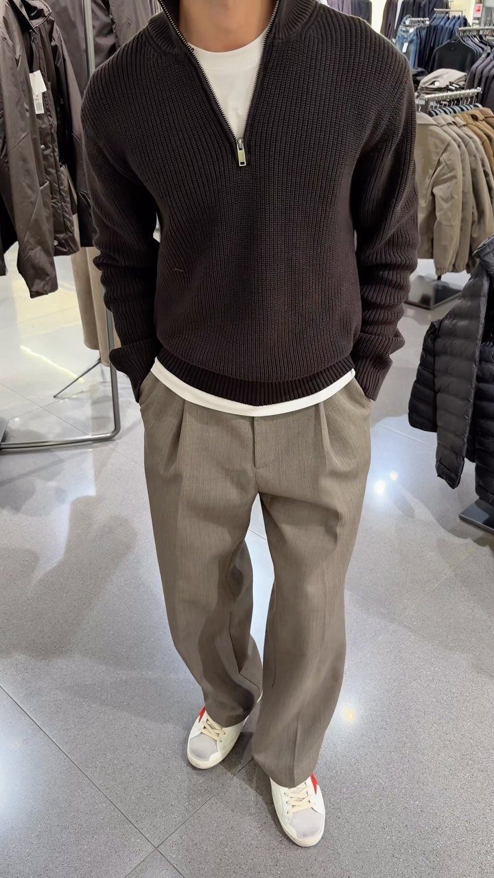 Man wearing a brown quarter-zip sweater, taupe dress pants, and white sneakers.