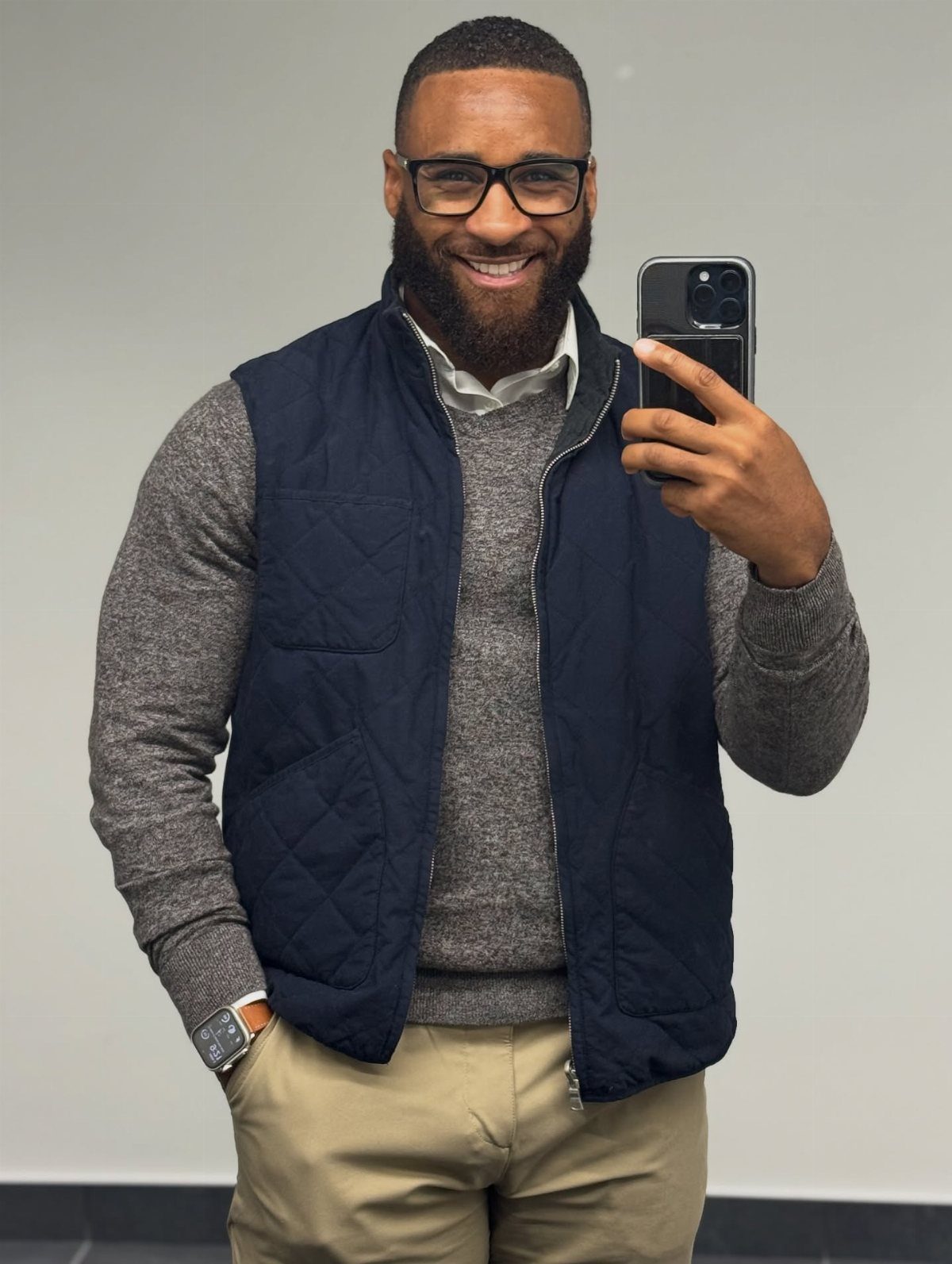 Man wearing a navy quilted vest over a grey sweater and khaki pants.