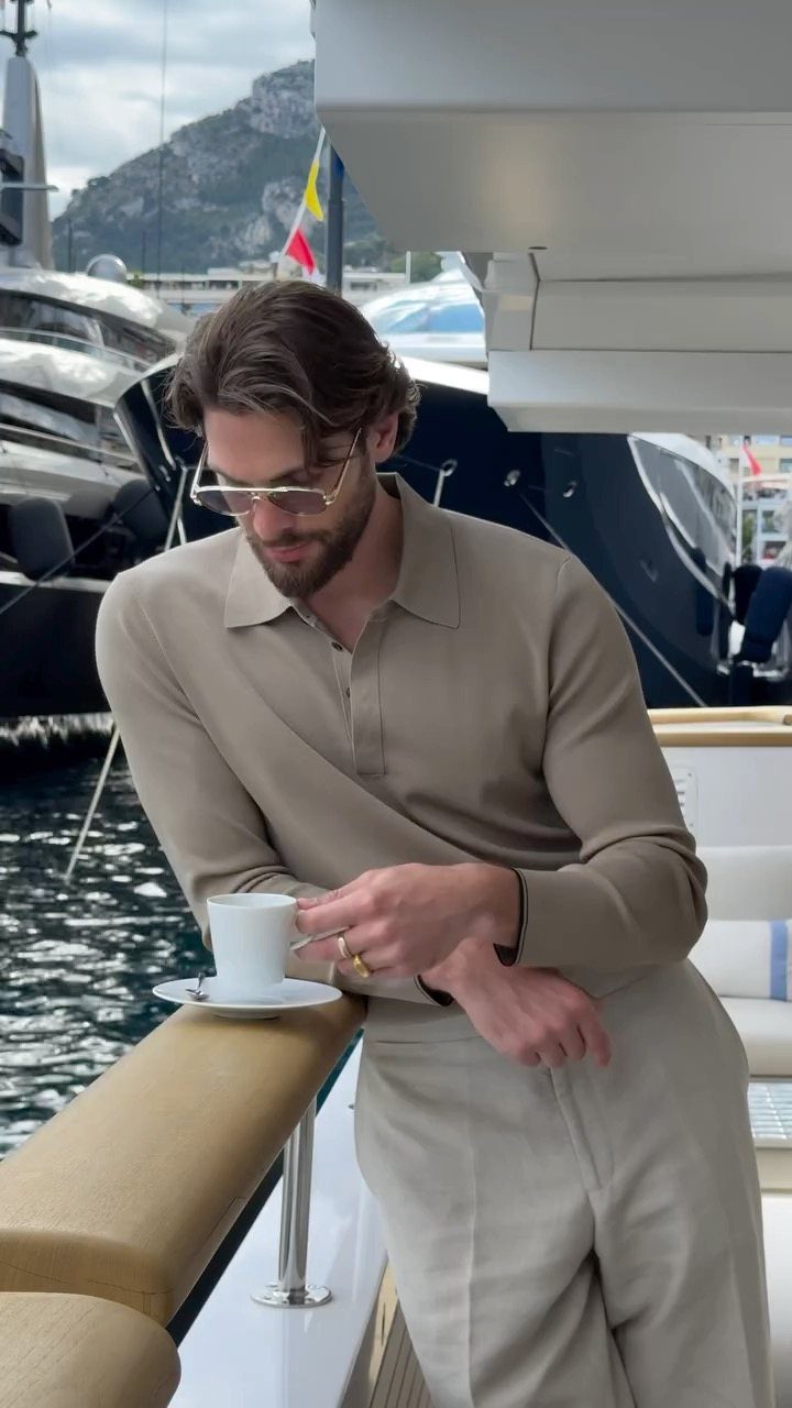Man in beige polo and trousers holding coffee on a luxury yacht deck
