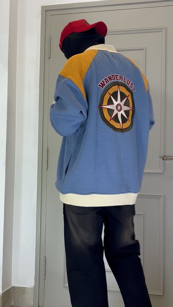 Person wearing a blue and yellow lightweight jacket with a compass graphic on back.