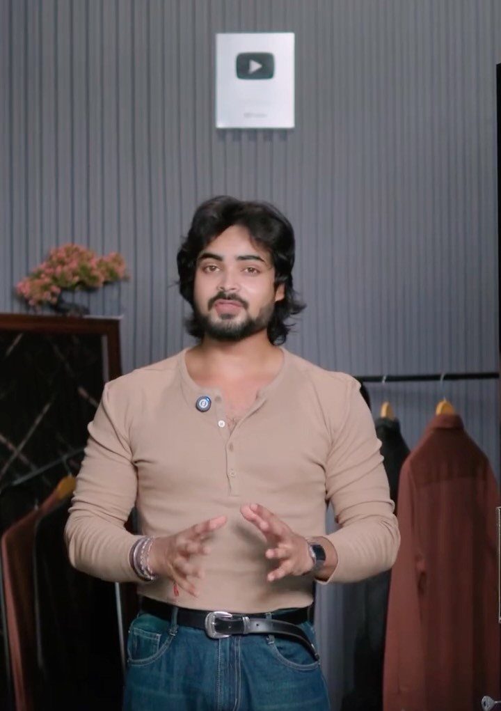 Man wearing a tan henley shirt and blue jeans standing in a studio
