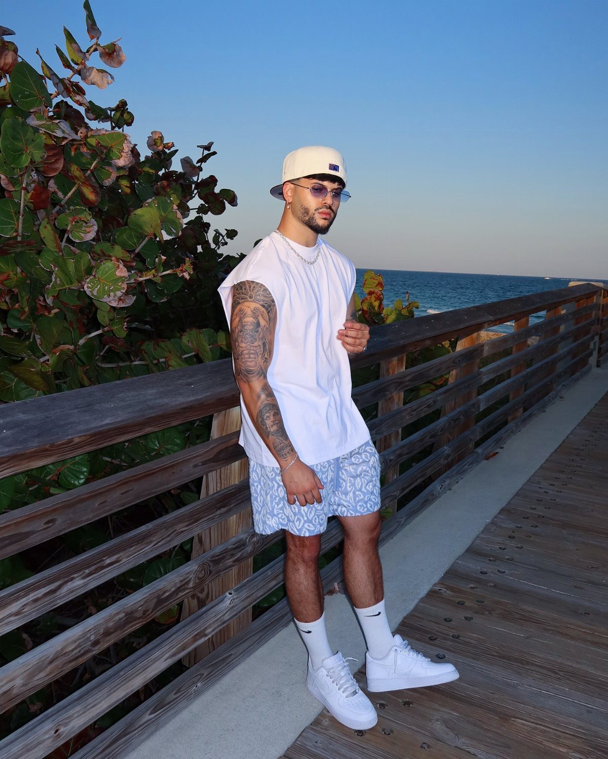 Man wearing white t-shirt and light blue patterned shorts on a wooden boardwalk.