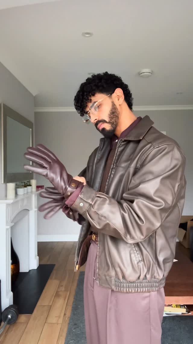 Man wearing a monochrome mauve leather jacket, trousers, and gloves in a room.