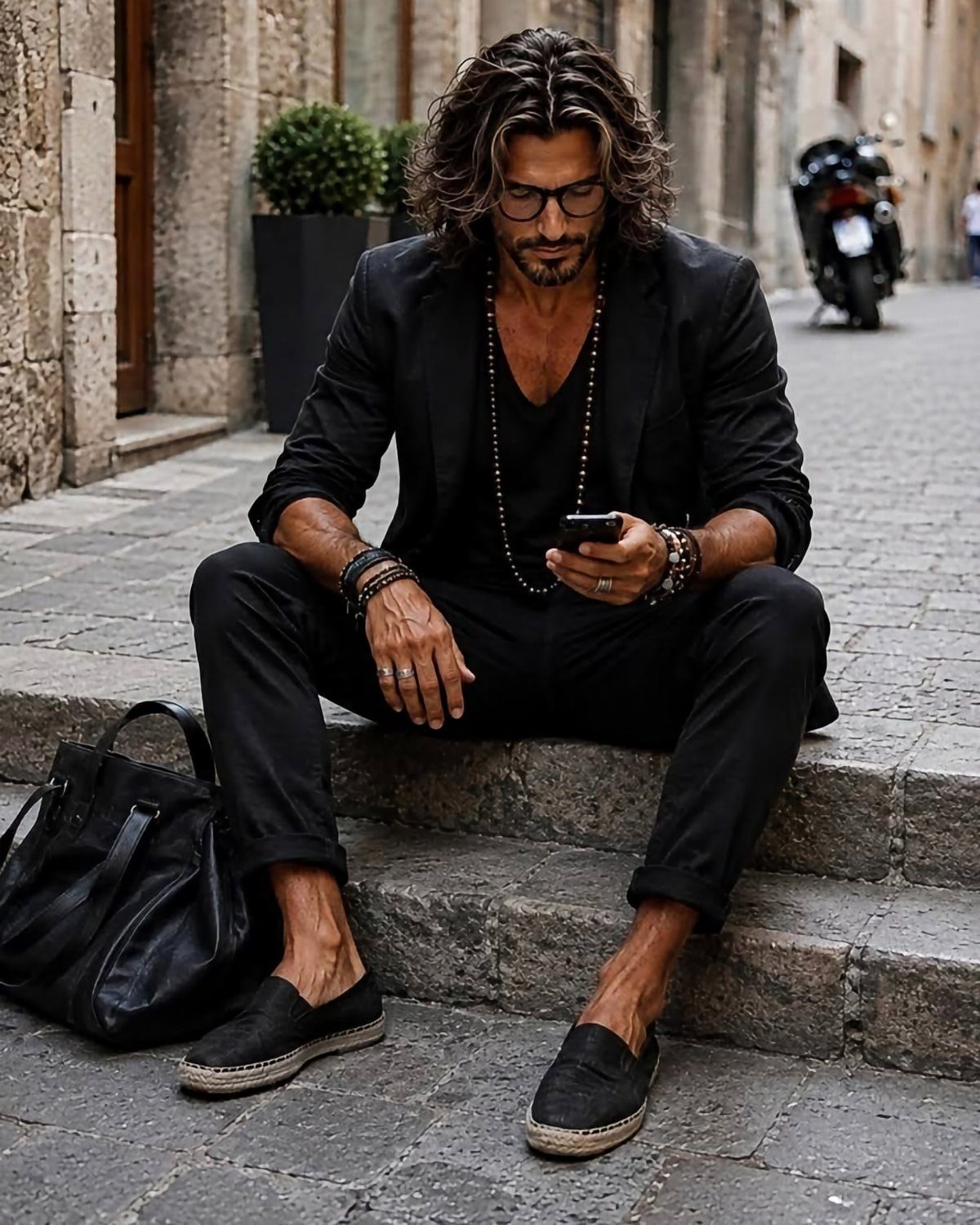 Man in all-black monochrome outfit sitting on stone steps in an outdoor setting