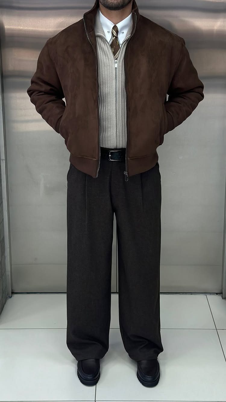 Man wearing a brown suede jacket, beige sweater, and dark brown wide-leg trousers.