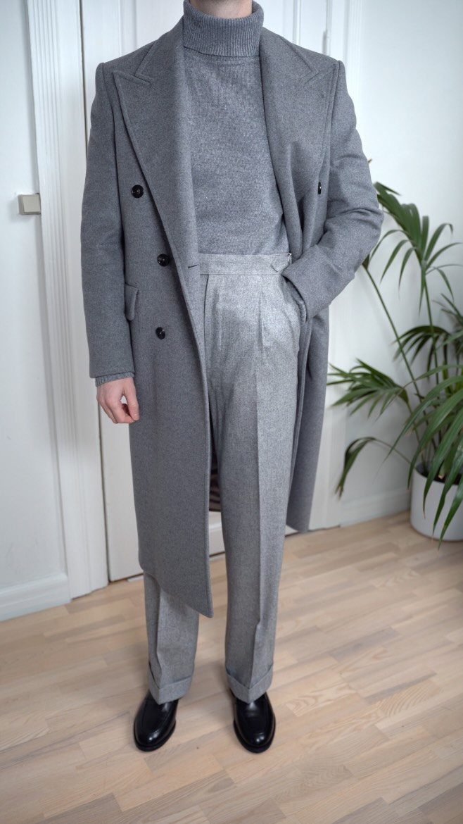 Man wearing a monochrome grey overcoat, turtleneck, and trousers with black shoes.