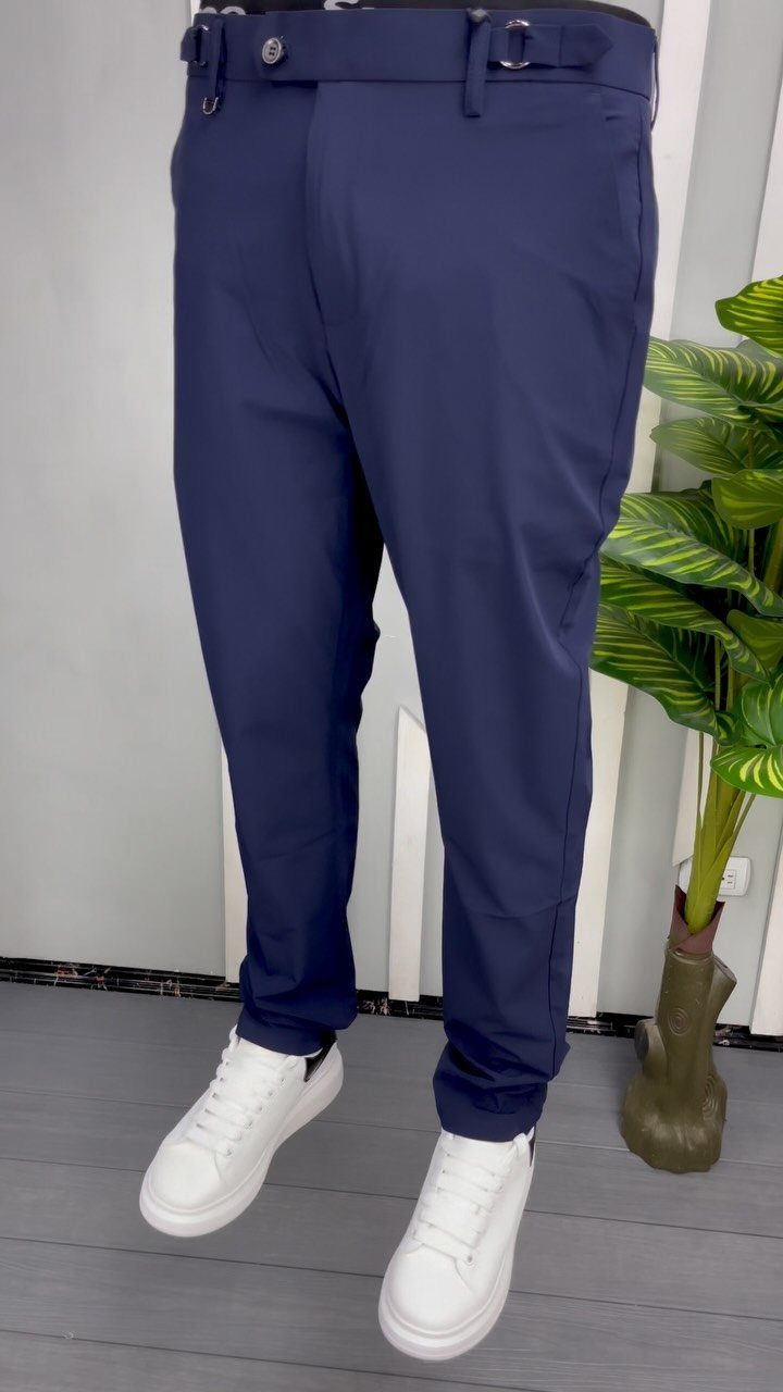 Navy blue trousers paired with clean white sneakers against a white wall.