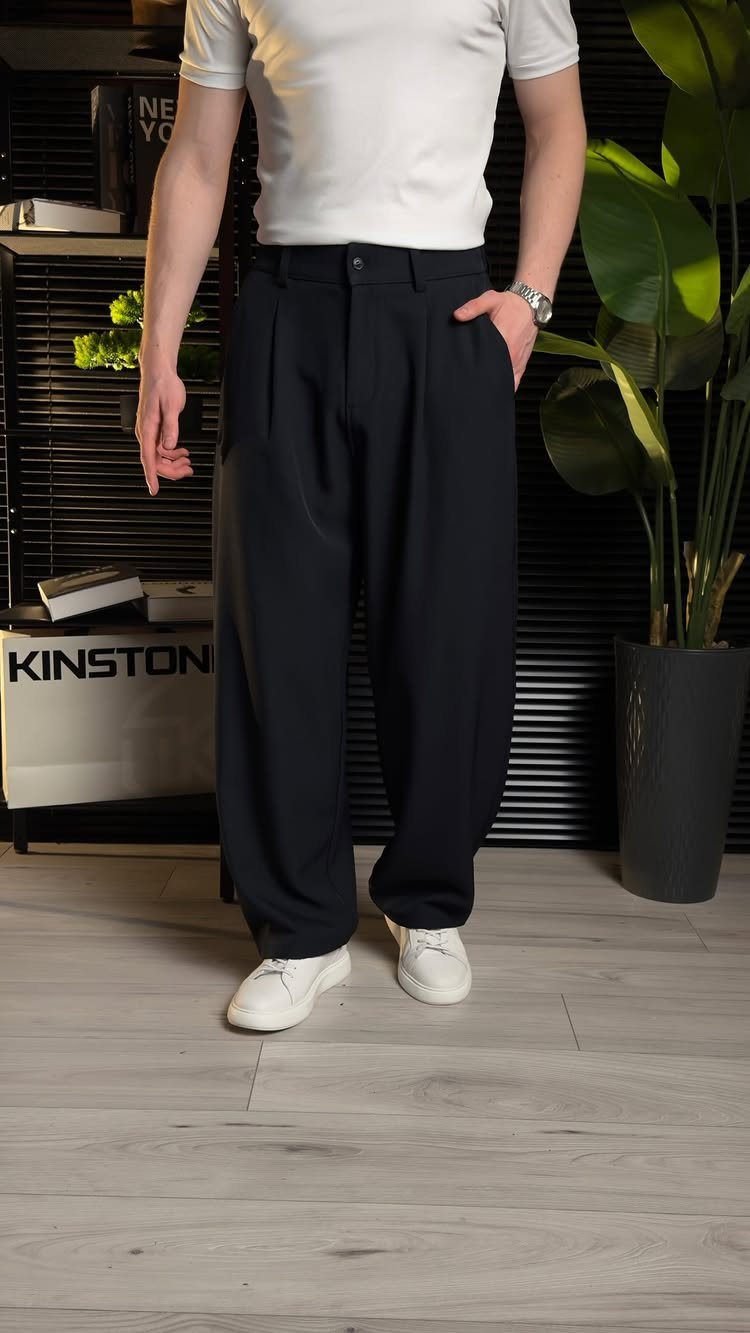 Person wearing white t-shirt, wide-leg navy blue trousers, and white sneakers indoors.
