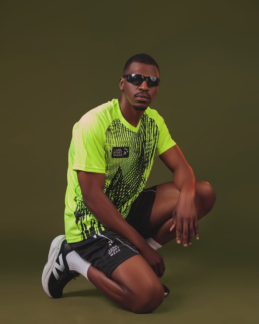 Man in neon yellow workout shirt and black shorts kneeling against green background