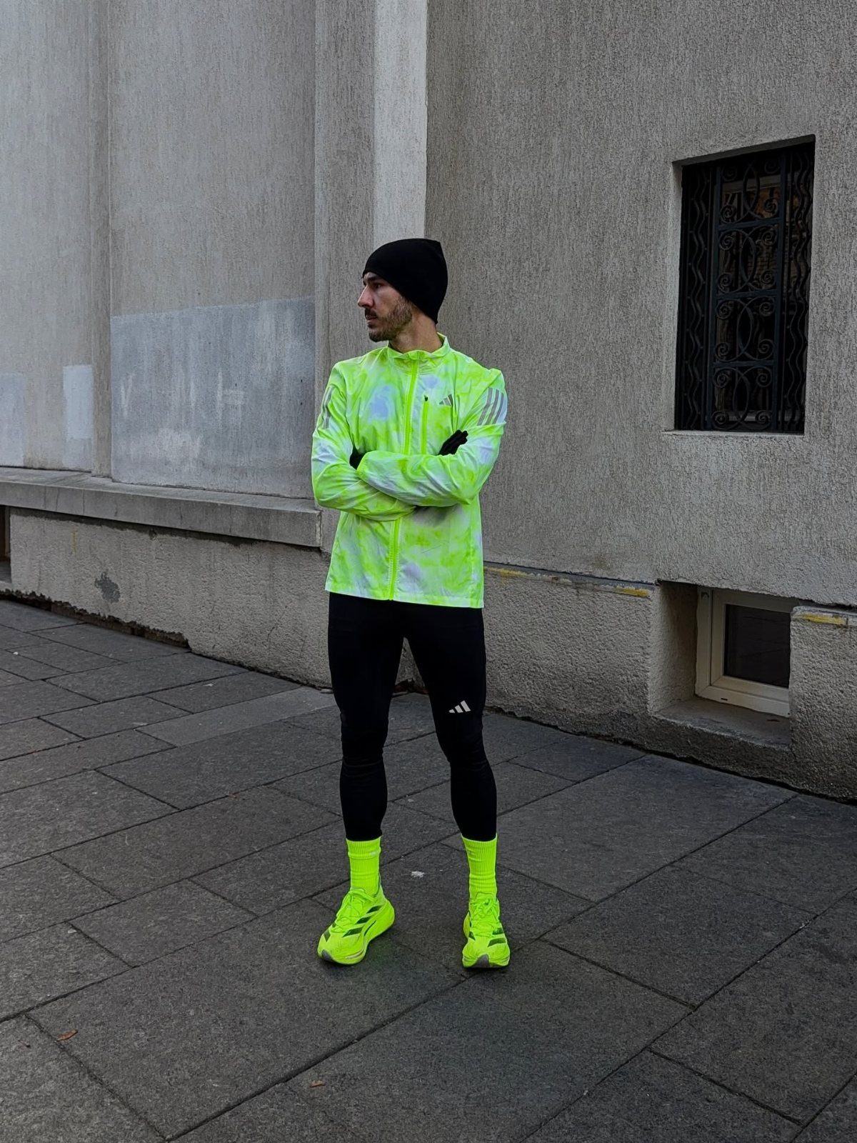 Man in neon tie-dye windbreaker, black leggings, and neon yellow sneakers outdoors.