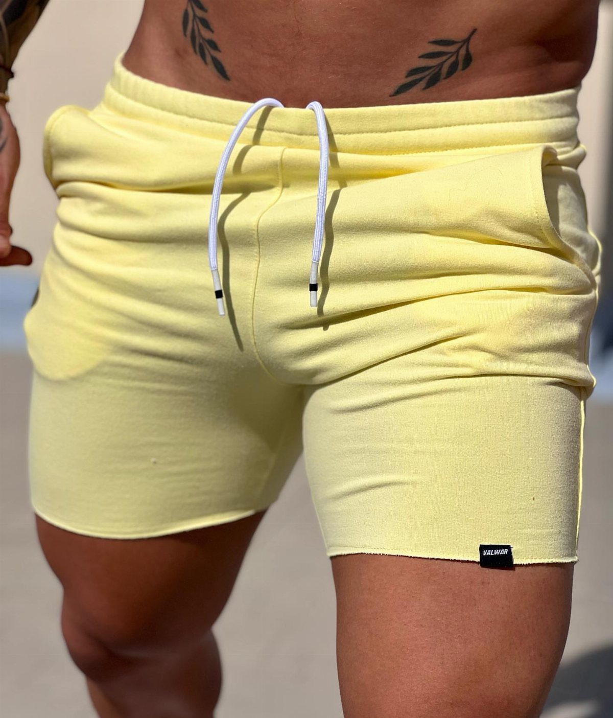 Neon yellow athletic shorts with white drawstrings worn by a person with tattoos.