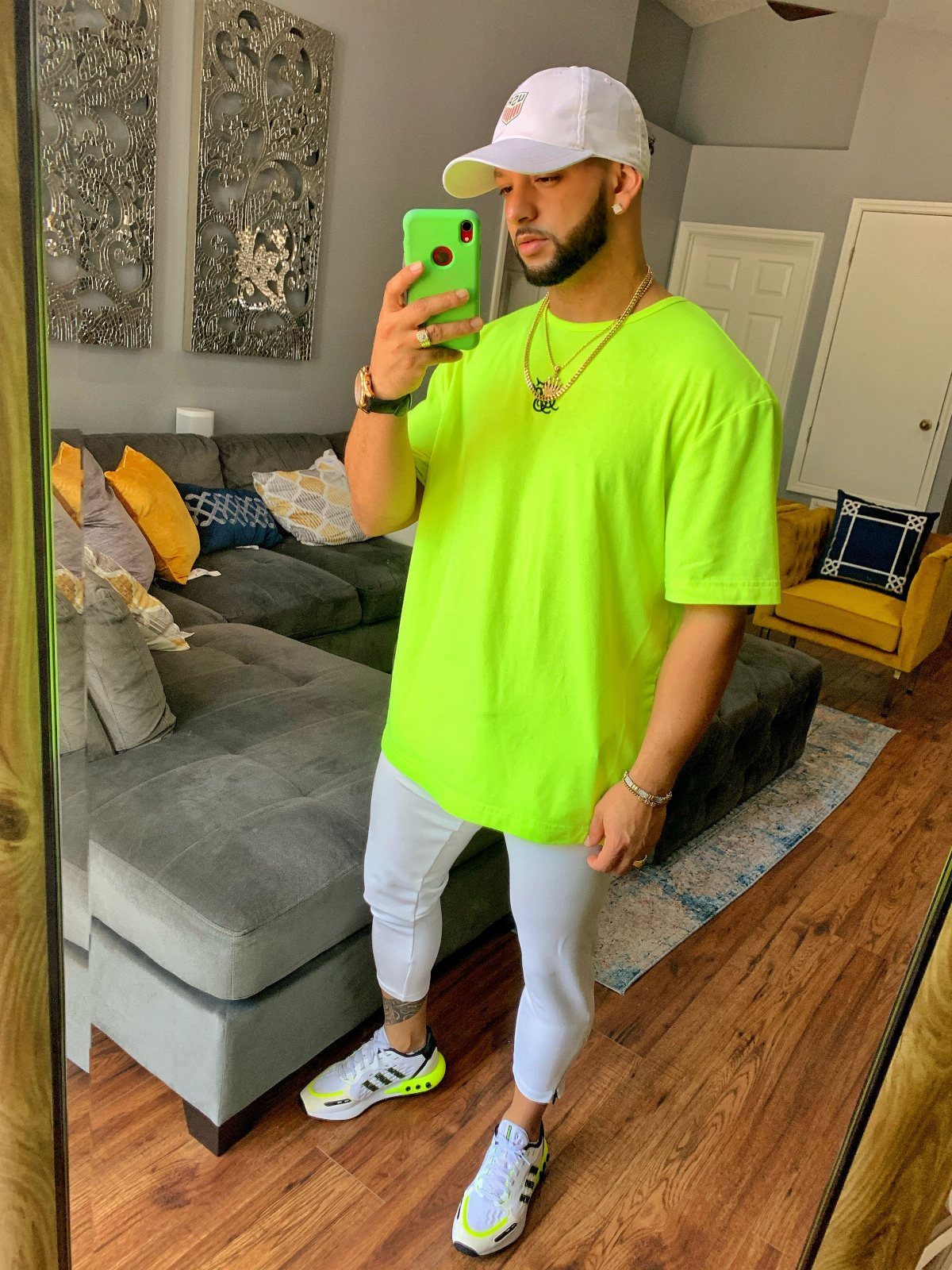 Man in neon yellow t-shirt and white leggings taking a mirror selfie.