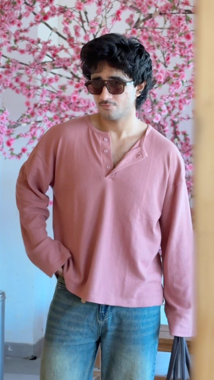 Man in a dusty rose henley shirt and blue jeans against pink blossoms.