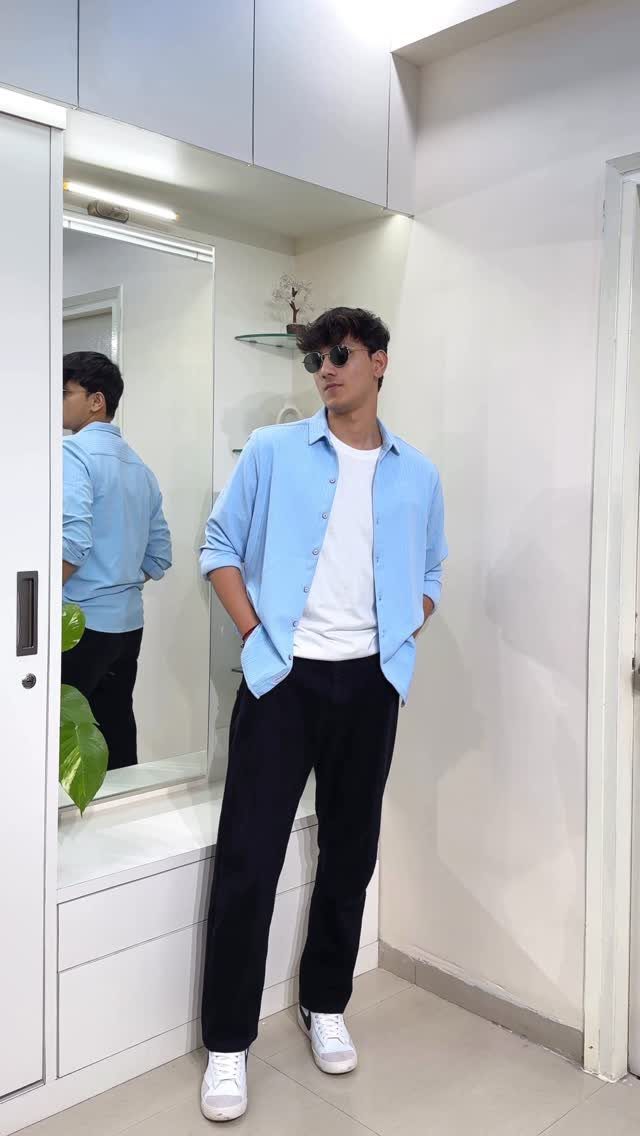 Young man wearing a light blue shirt, white t-shirt, and black trousers.