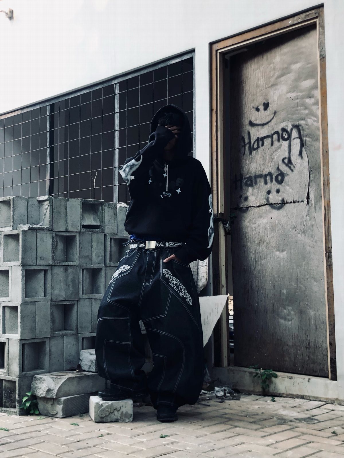 Person in black oversized hoodie and baggy black cargo pants standing by concrete wall