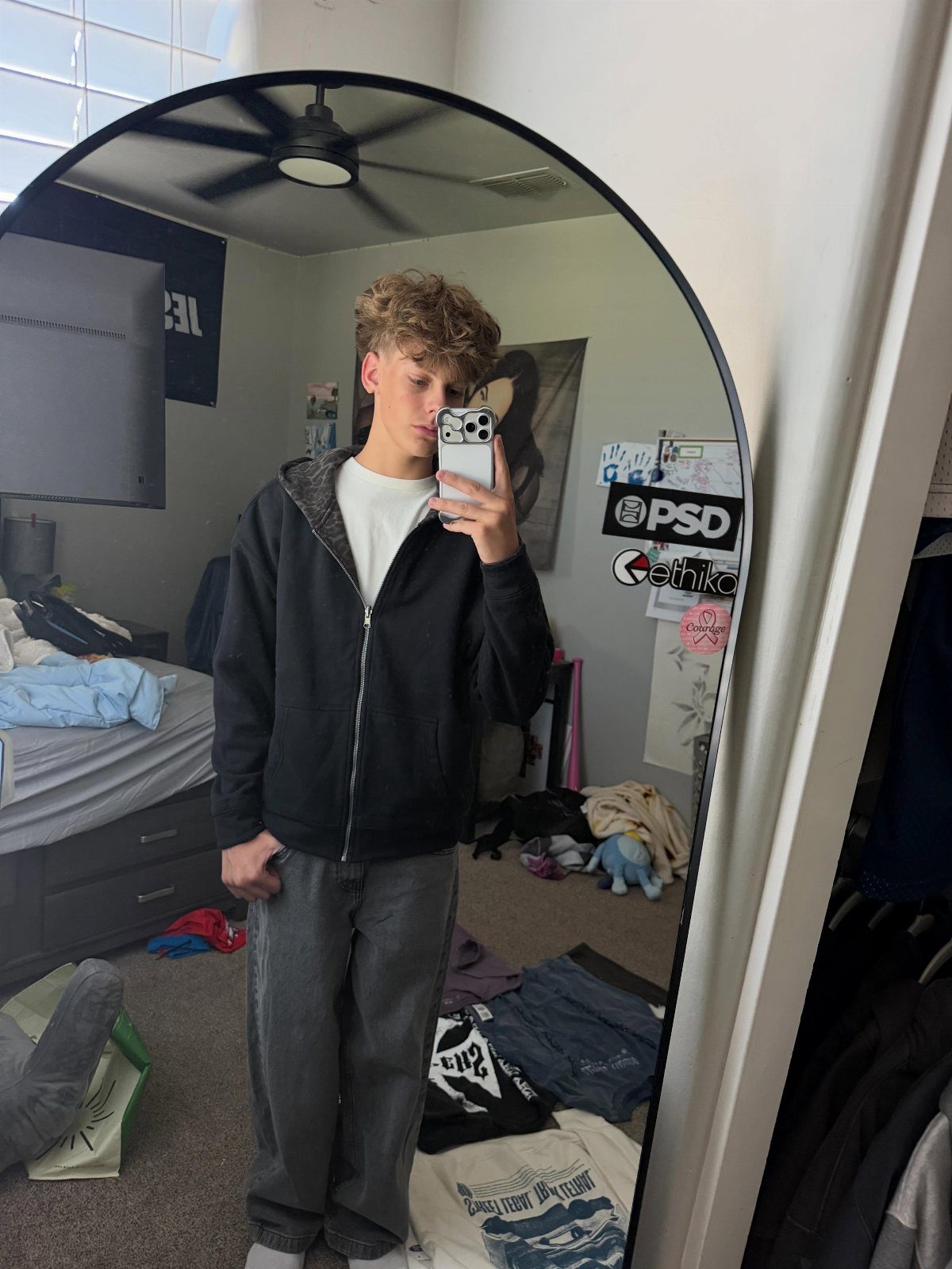 Teenage boy in black zip-up hoodie and grey trousers taking a mirror selfie.