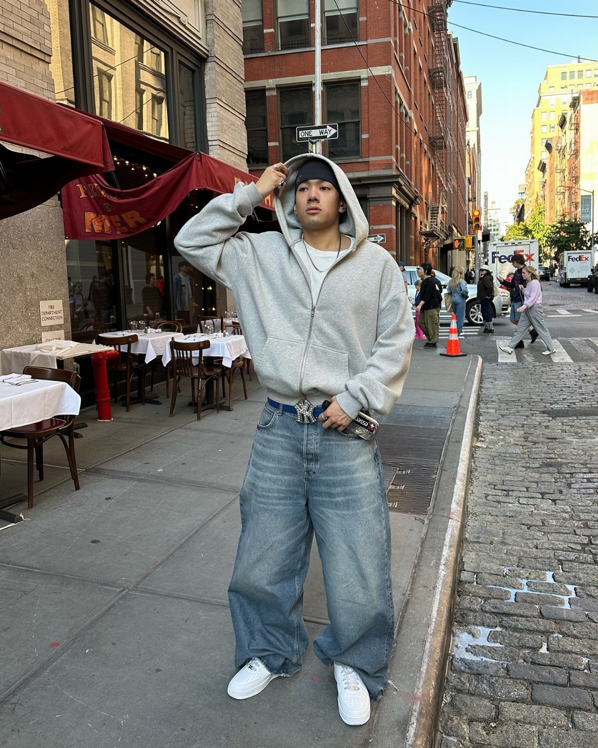Person in oversized grey hoodie and baggy blue jeans on a city street