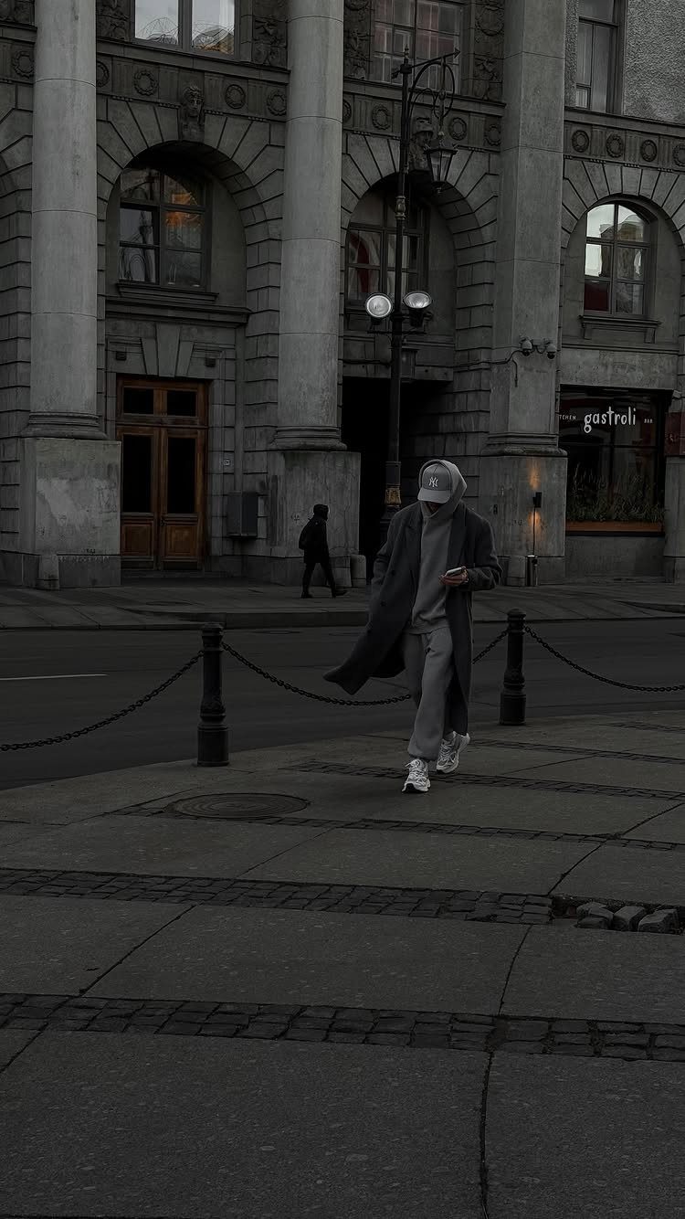 Person in a long black coat and grey hoodie walking on city street