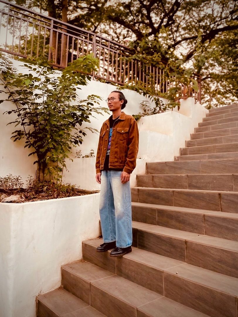Person wearing a rust corduroy jacket and wide-leg jeans standing on stone stairs.