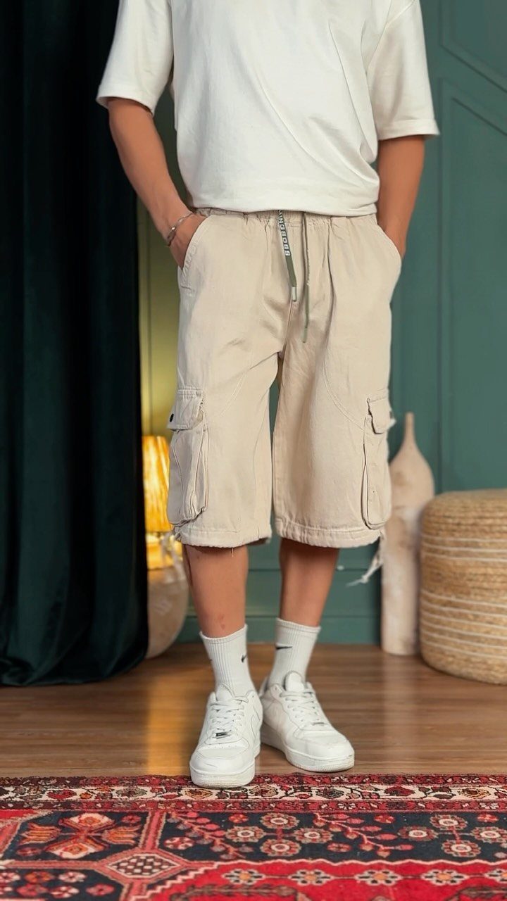 Person wearing a white t-shirt and beige long cargo shorts with white sneakers.