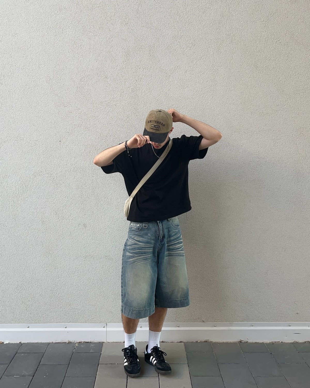 Person wearing long light-blue denim shorts, black t-shirt, and tan baseball cap.