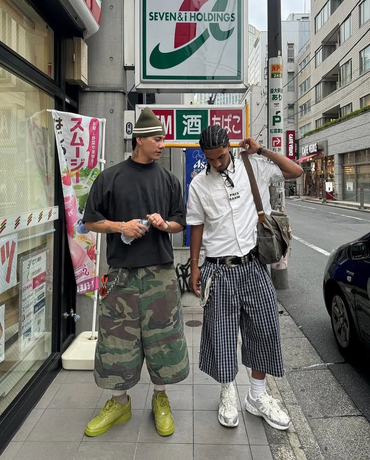Two men in streetwear wearing long shorts that cover the knee on a sidewalk