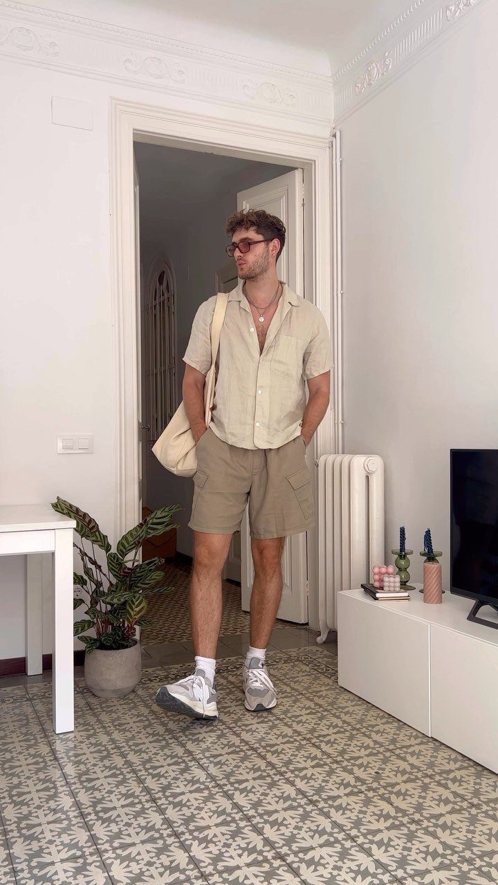 Man wearing a beige shirt and tan long shorts with white sneakers indoors