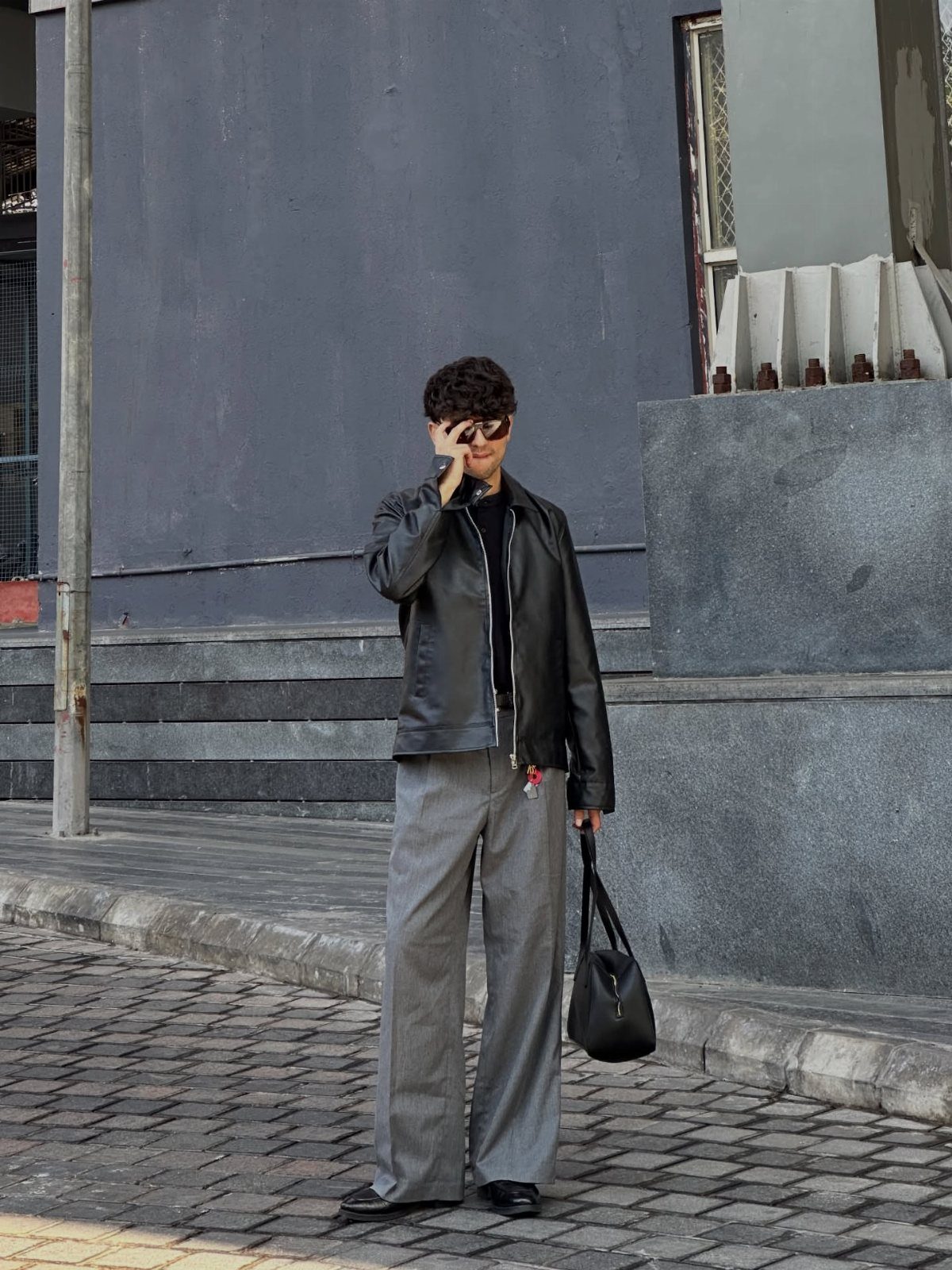 Person wearing a black leather biker jacket and wide-leg grey pinstripe pants.