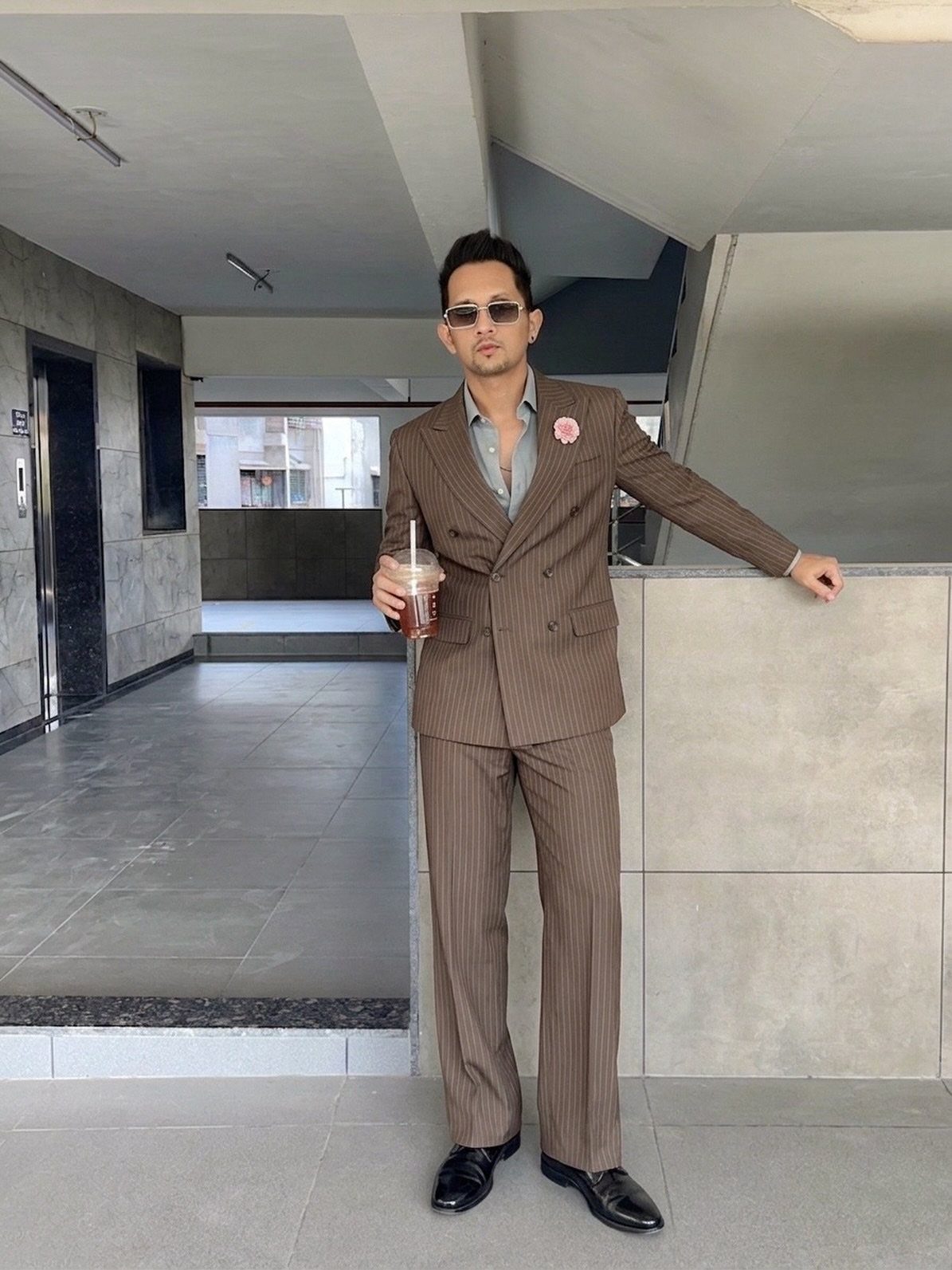 Man in a tan double breasted pinstripe suit and sunglasses in a hallway