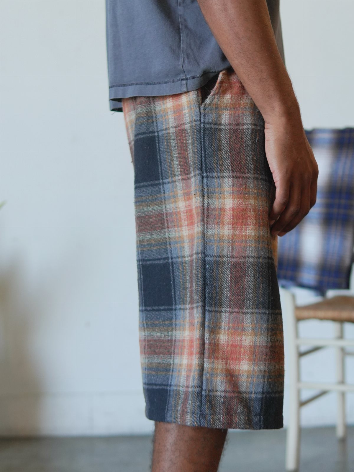 Person wearing grey t-shirt and blue and orange plaid knee-length shorts.