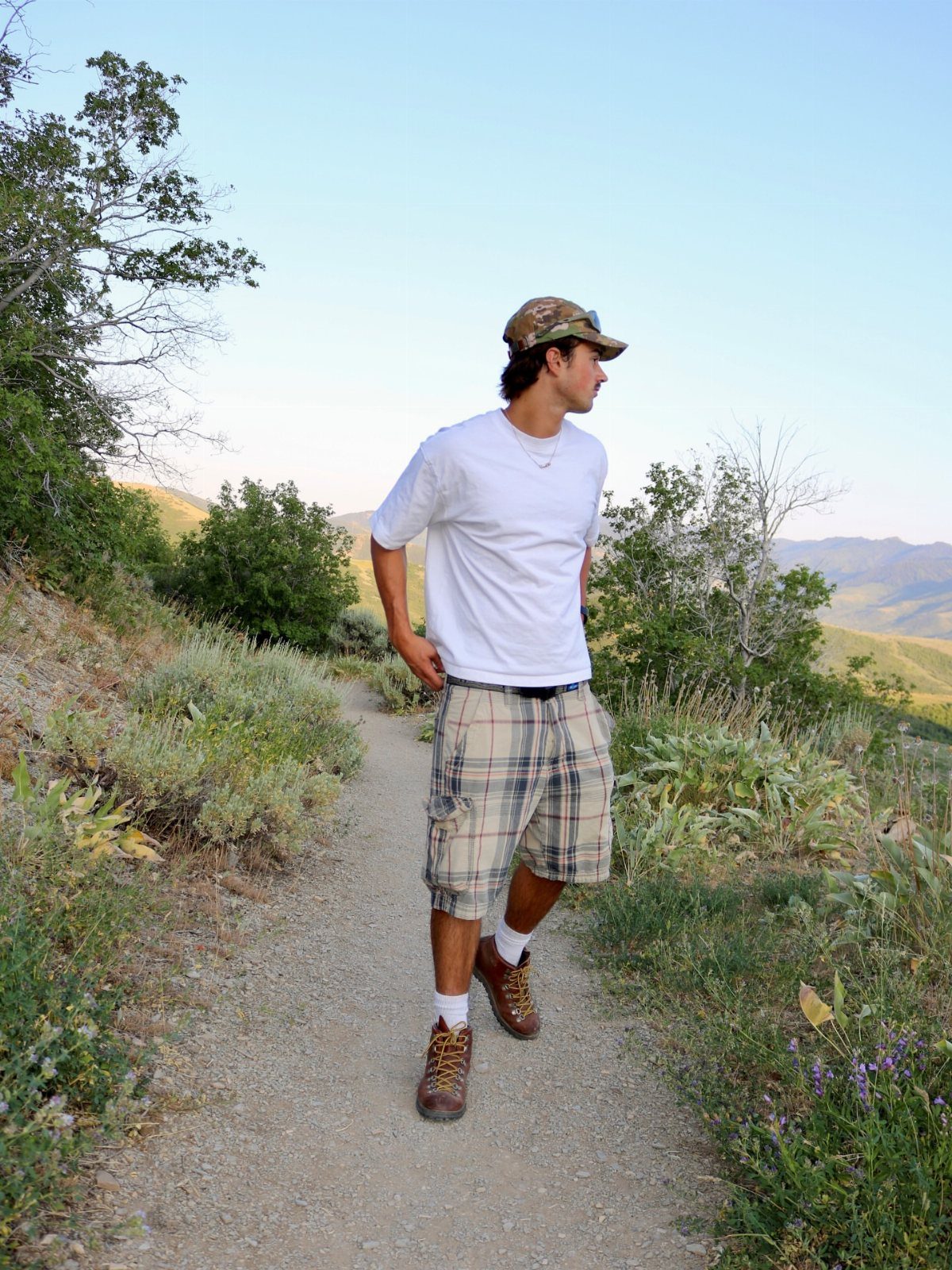 Man wearing a white t-shirt and plaid cargo shorts walking on a trail