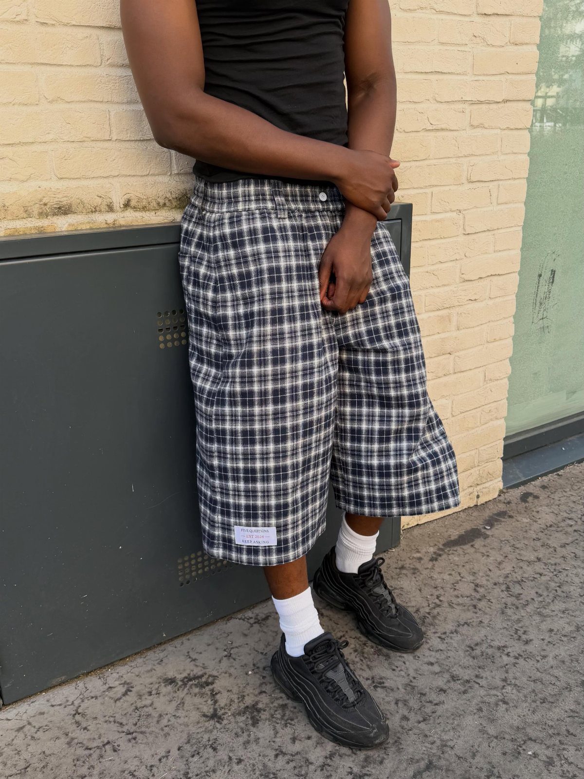 Person wearing black shirt, blue plaid wide-leg shorts, white socks, and black sneakers.