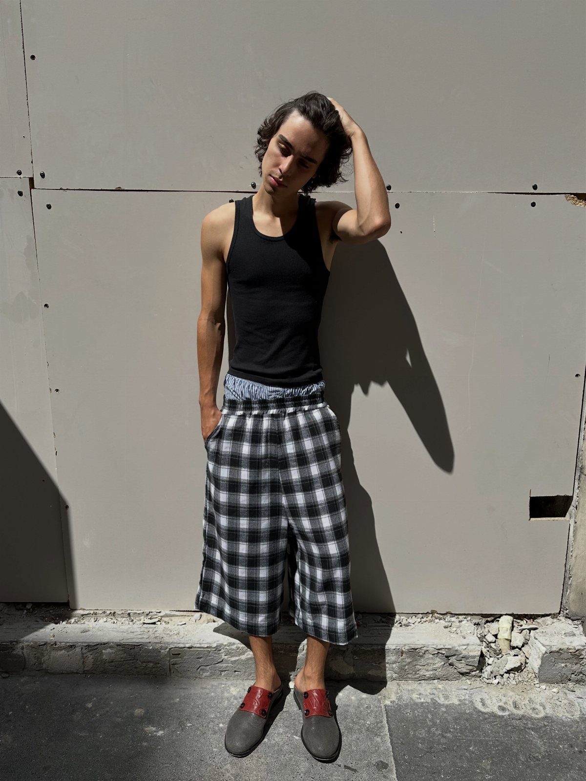 Man wearing a black tank top and wide-leg black and white plaid cropped trousers.