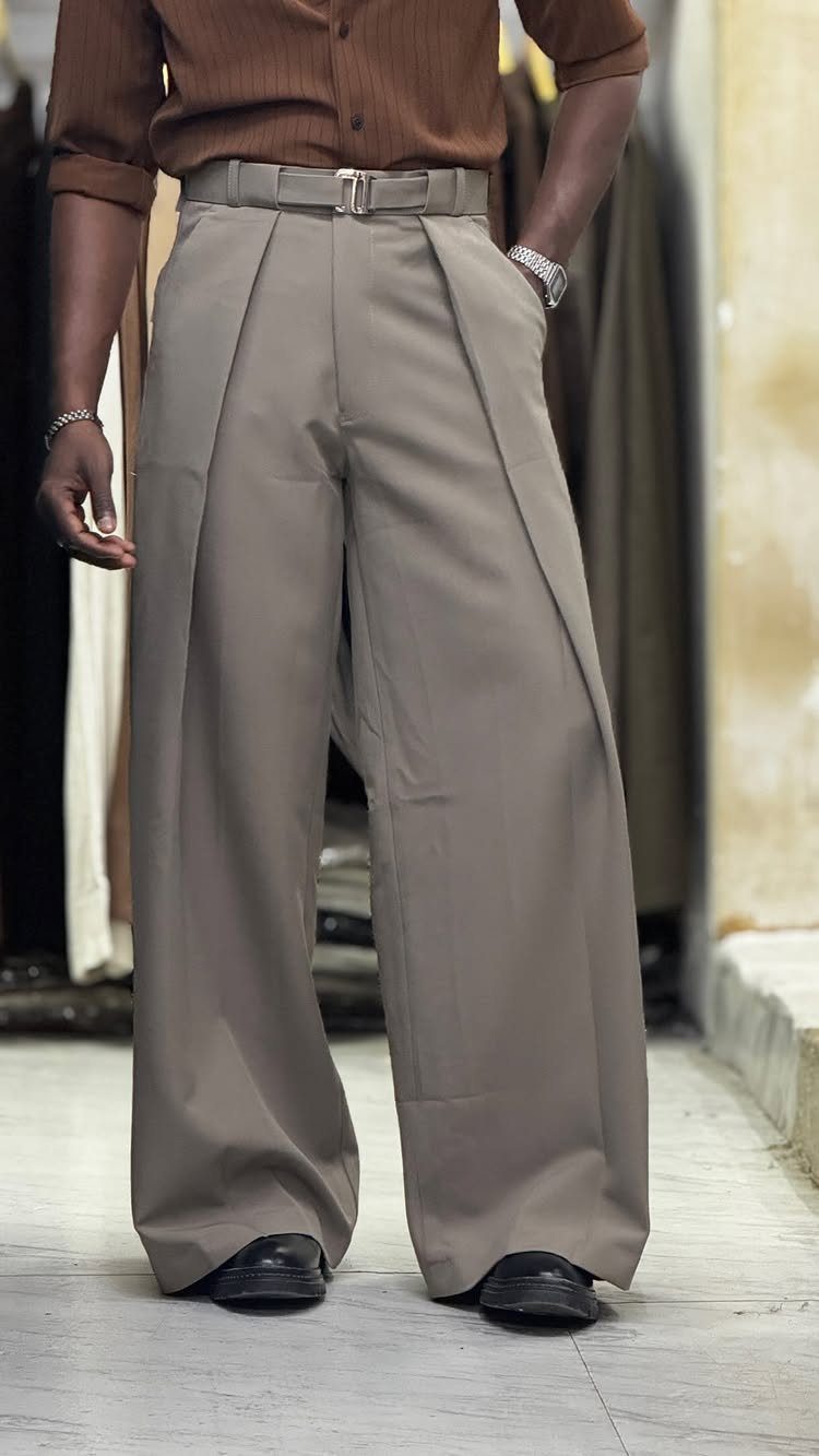 Person wearing wide-leg taupe pleated pants with a brown shirt and black shoes.