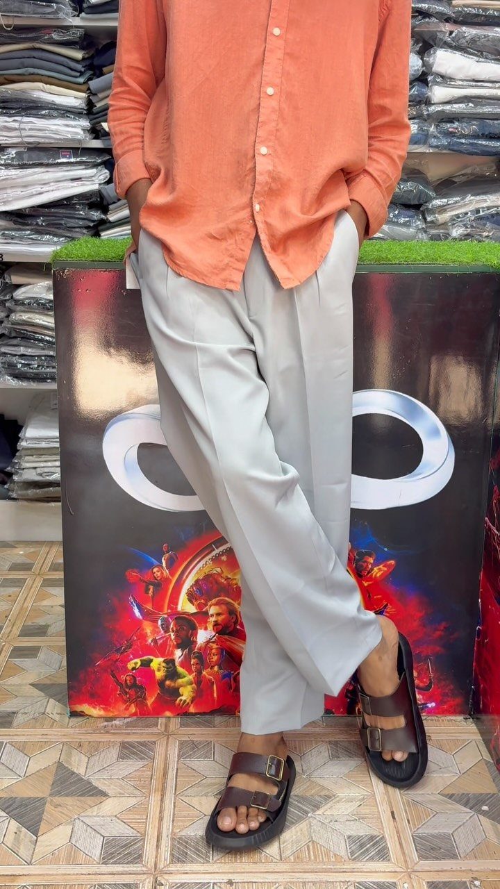 Person wearing an orange shirt and light grey pleated pants with brown sandals.
