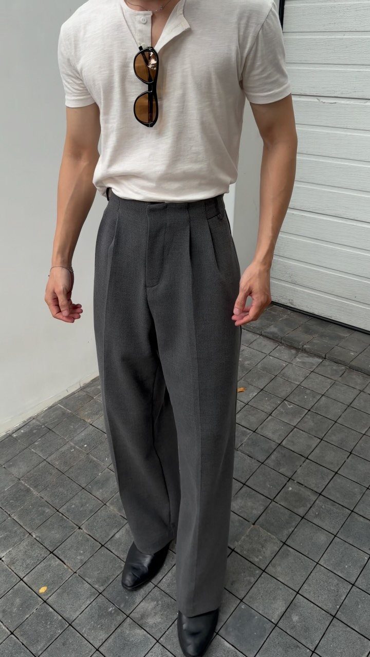 Person wearing a white polo shirt and charcoal grey pleated trousers with black shoes.