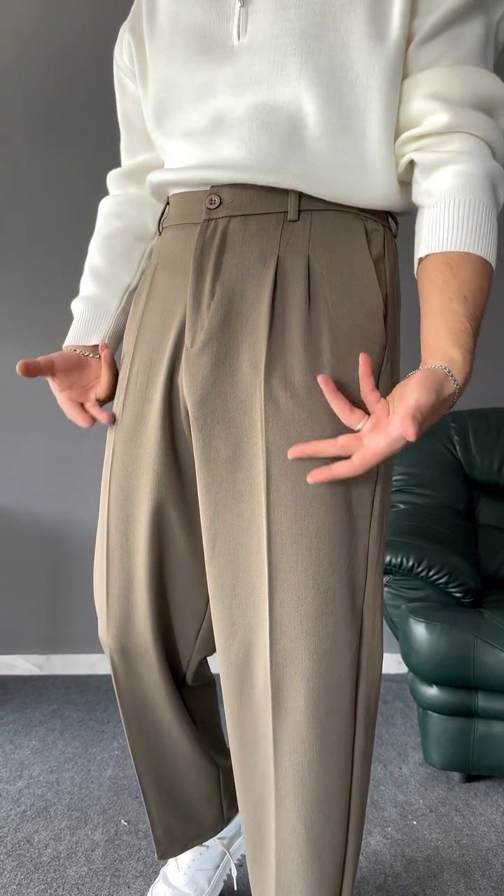 Person wearing a white sweater and olive-brown wide-leg pleated trousers indoors.