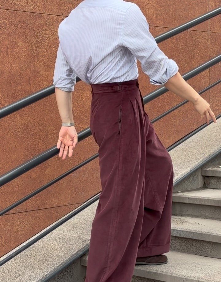 Person wearing burgundy wide-leg pleated trousers and a tucked-in light shirt on stairs.