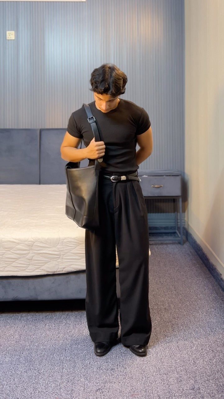 Man wearing a black tucked-in t-shirt, black belt, and wide-leg pleated trousers.