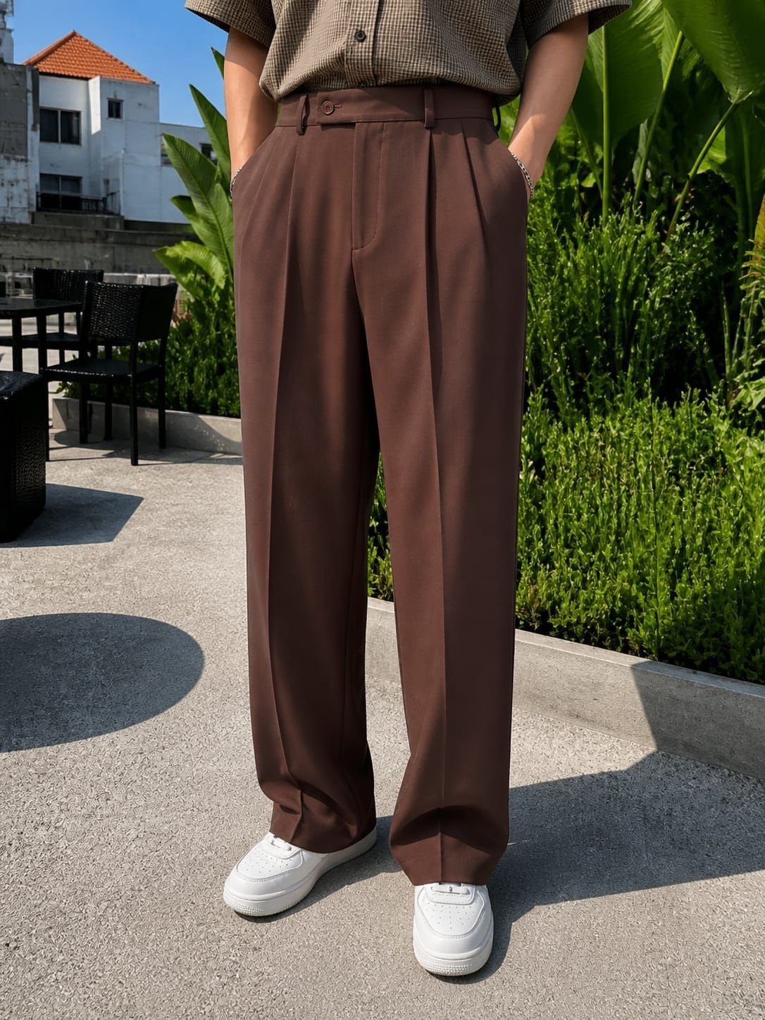 Brown wide-leg pleated trousers paired with a patterned shirt and white sneakers outdoors.