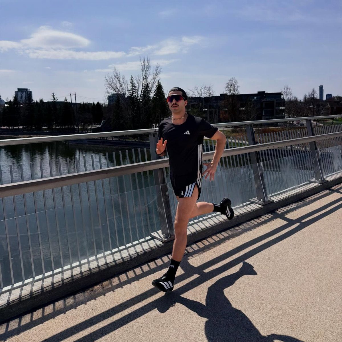 Man running on a riverside path wearing a black athletic outfit and sunglasses.