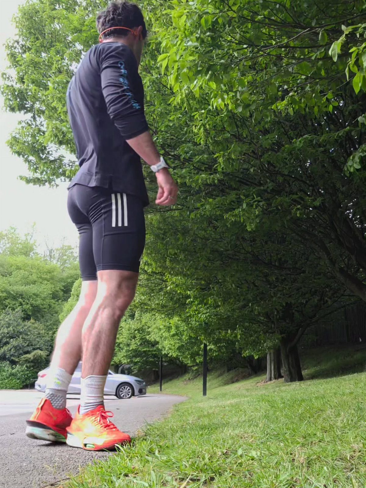Man in black long-sleeve shirt and tight black sports shorts standing outdoors.