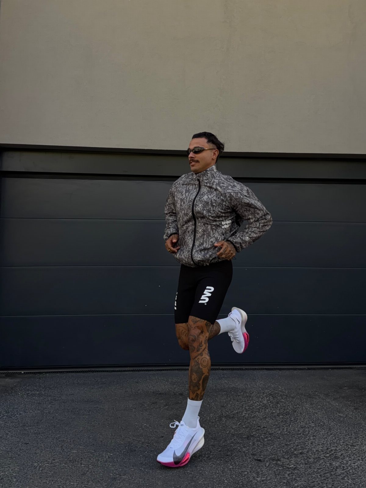 Man running in a grey patterned jacket and black athletic shorts outdoors.