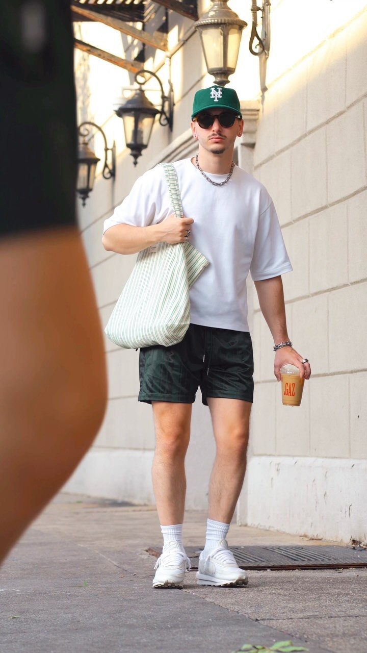 Man wearing a white crew-neck t-shirt and dark green sports shorts on a sidewalk