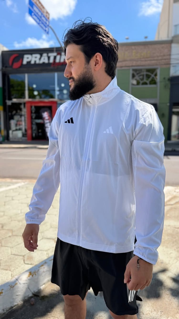 Man wearing a white athletic jacket and black running shorts on a city street.