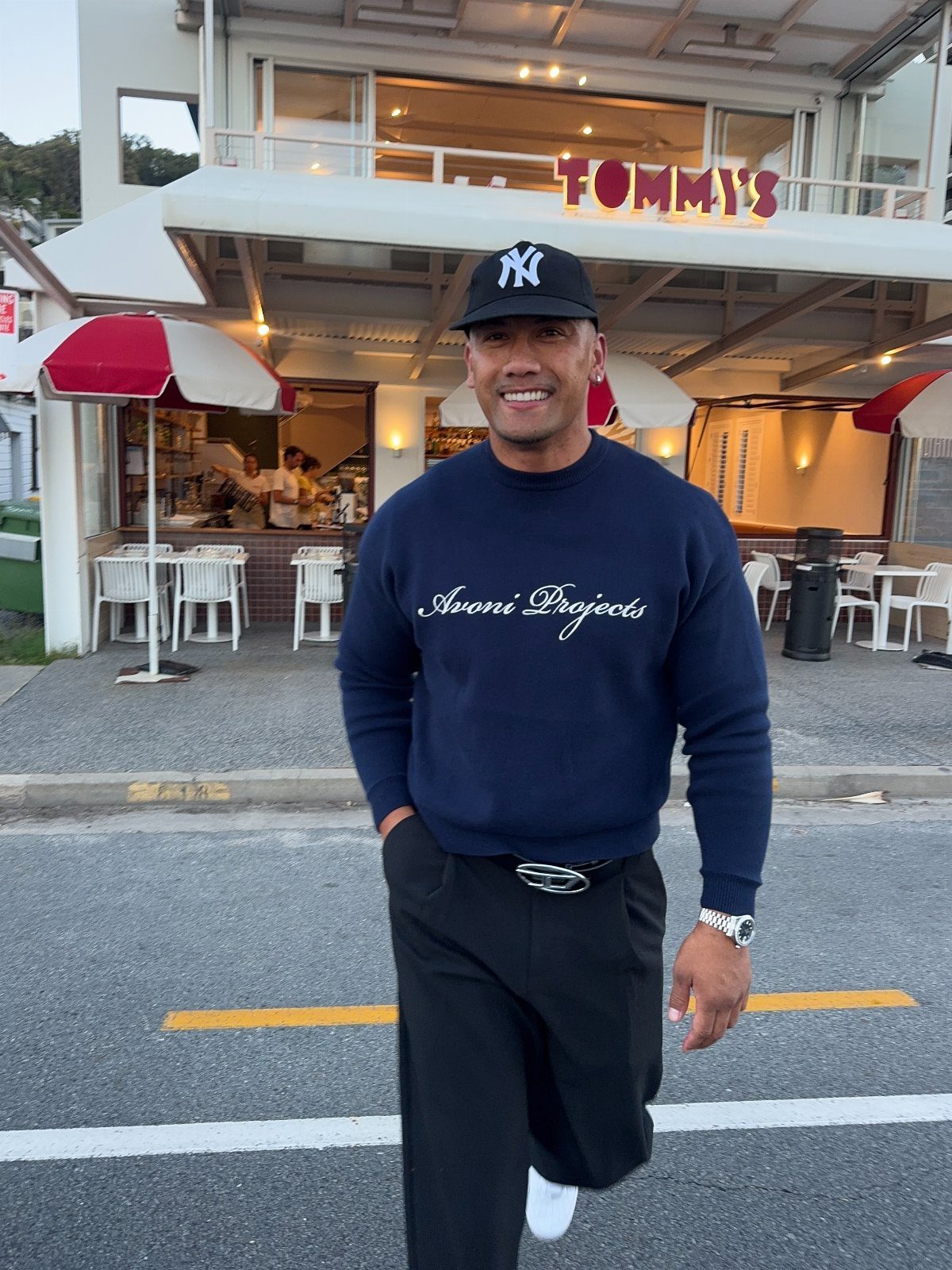 Man wearing navy crewneck sweatshirt, black trousers, and New York Yankees baseball cap.