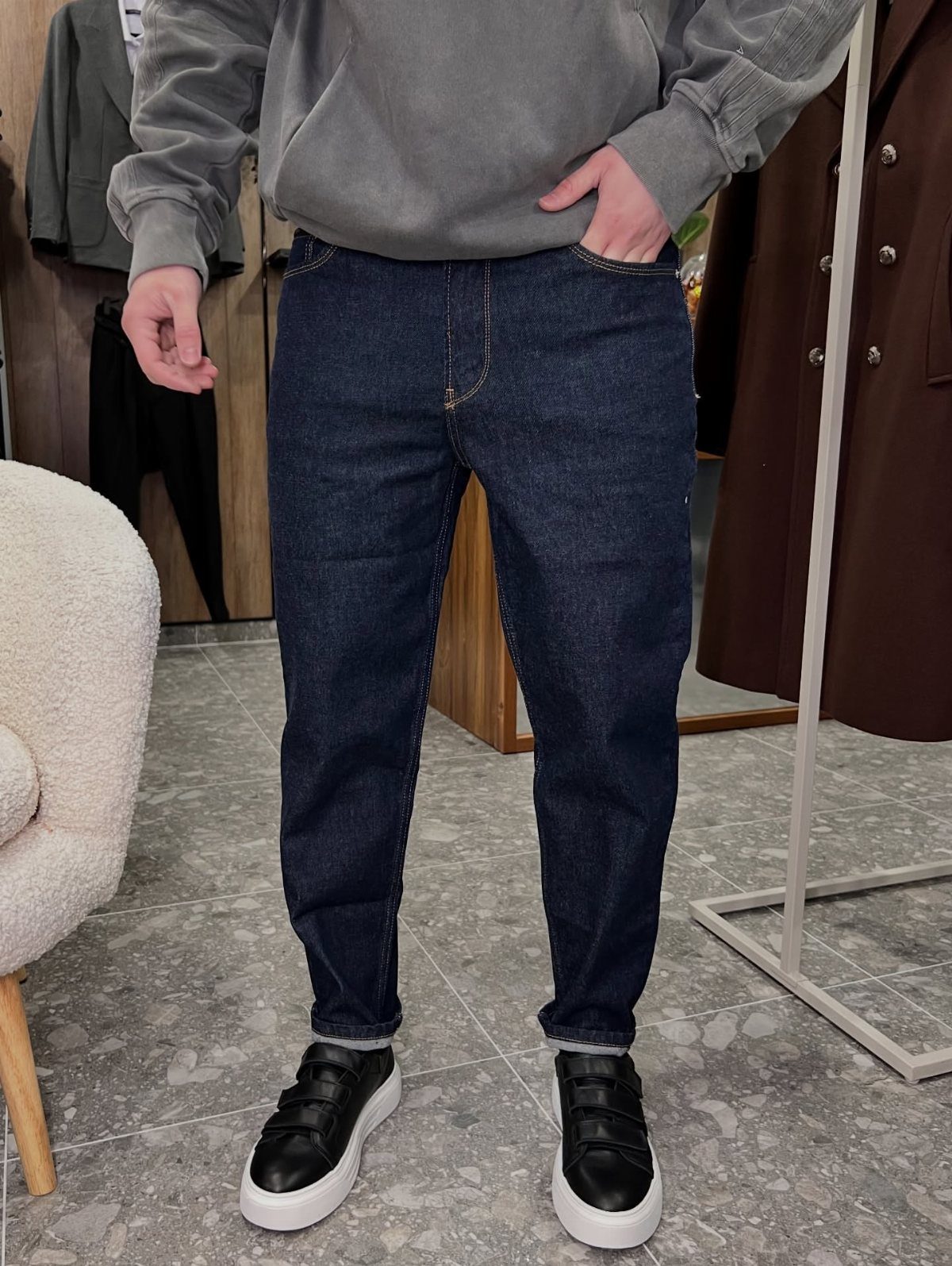 Person wearing a grey sweatshirt, dark blue jeans, and black sneakers in store.
