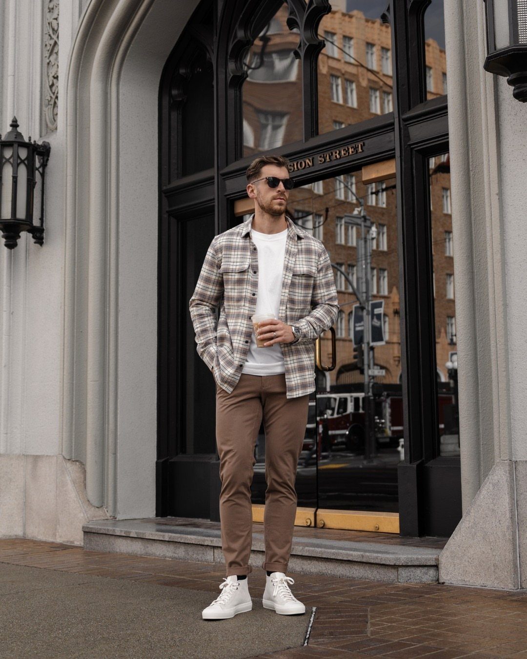 Man wearing a plaid shirt over a white tee with brown chinos and sneakers.